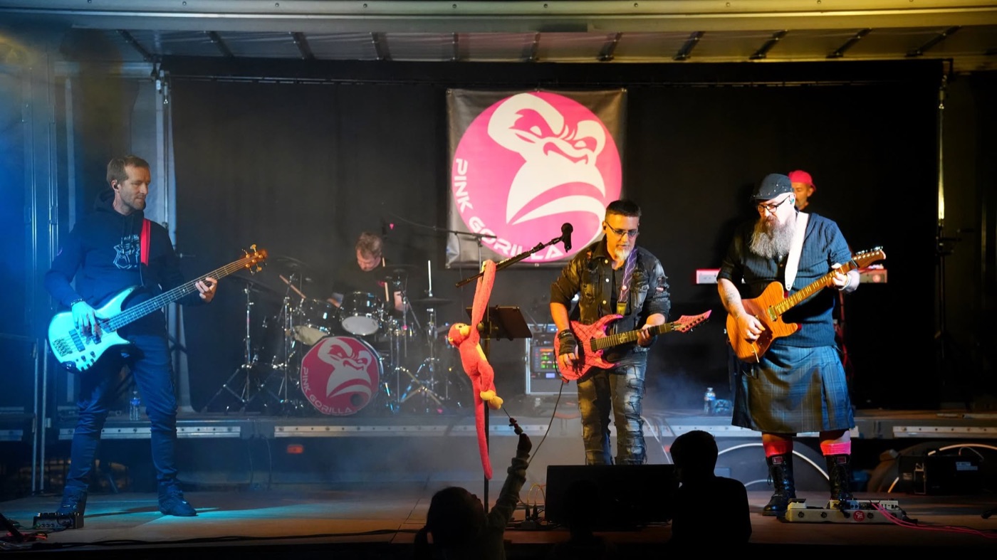 PINK GORILLA au complet sur scène : basse, batterie, guitares et clavier devant le logo du groupe.