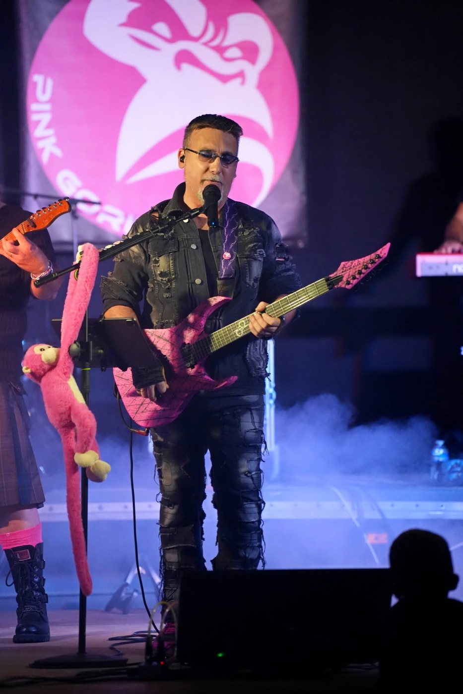 Chanteur et guitariste de PINK GORILLA au micro, avec une guitare rose devant le logo du groupe.