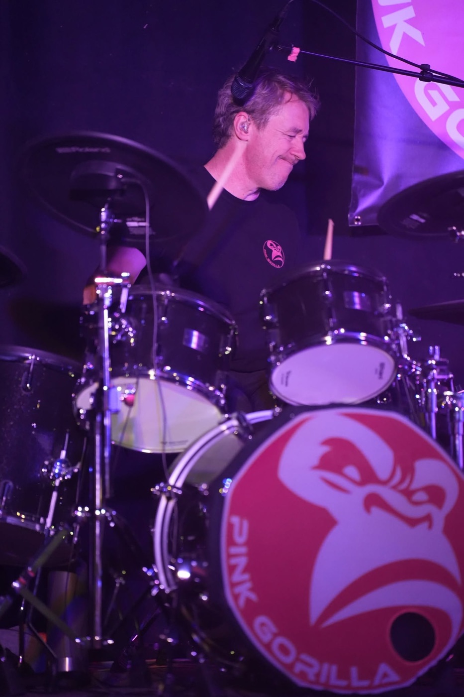Batteur de PINK GORILLA derrière sa batterie, dont la grosse caisse porte le logo rose du groupe.