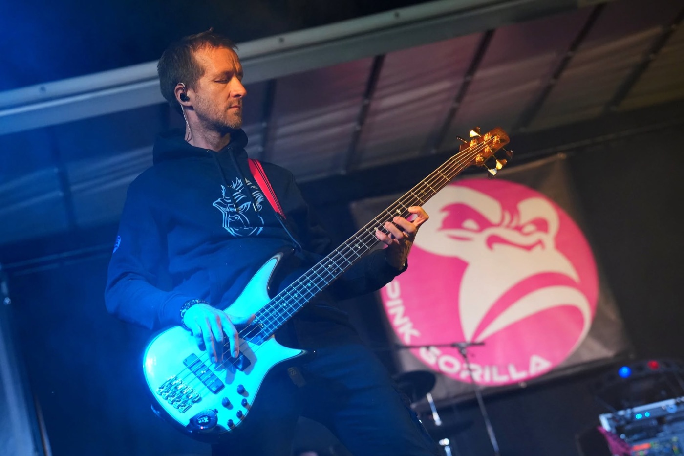 Bassiste de PINK GORILLA jouant une basse blanche devant le logo du groupe, sous les lumières bleues.