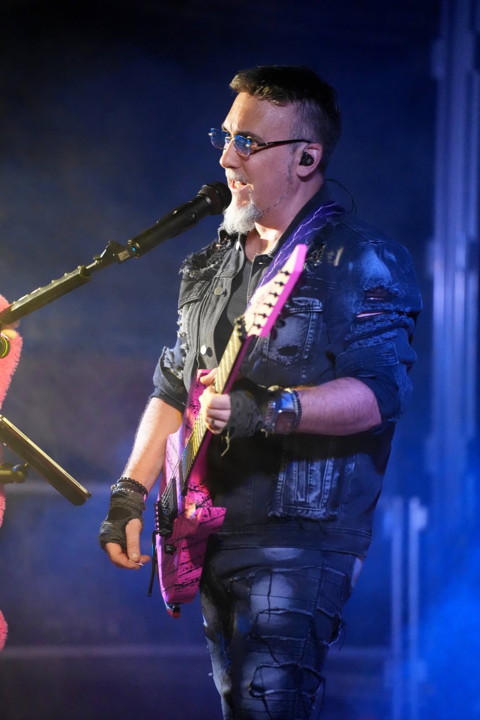Chanteur et guitariste de PINK GORILLA au micro, avec sa guitare rose sous les éclairages de concert.