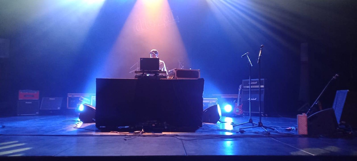 DJ Fabio derrière sa régie, sur une scène éclairée en bleu et ambre.